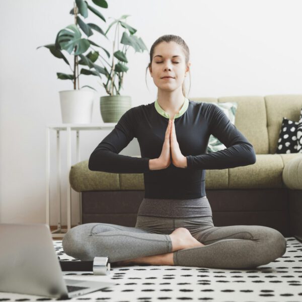 Young fit women doing yoga and stretching from home following a video on her laptop